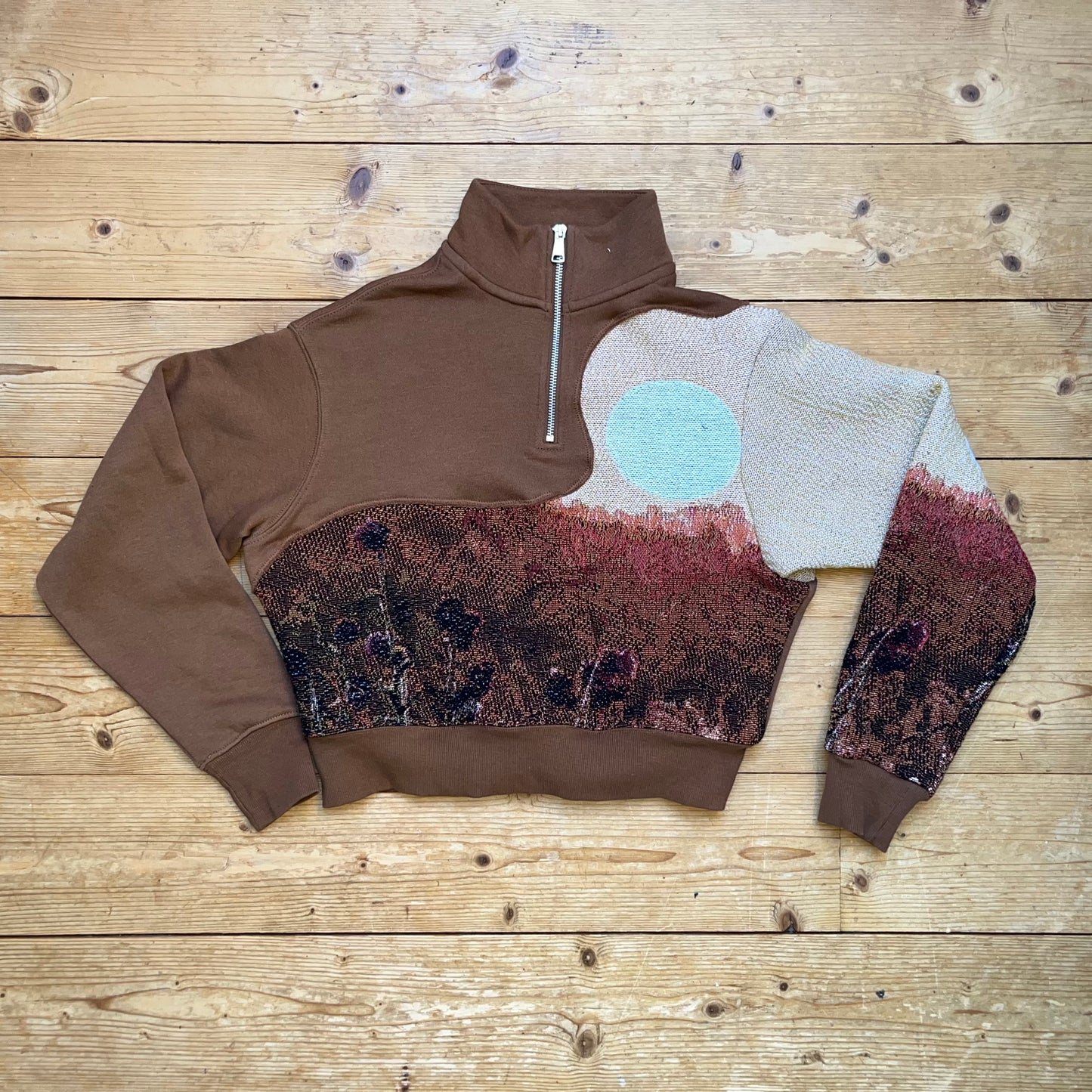 Brauner Secondhand Half-Zip Pullover mit handvernähtem Solar Flower Motiv von Sun Seam Studio – Vorderansicht flach liegend auf Holzboden, Recrafted Kollektion, Unikat aus 100% Baumwolle