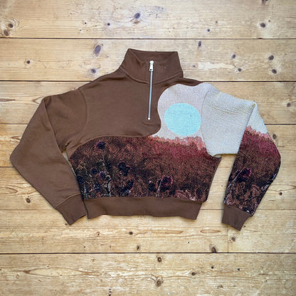 Brauner Secondhand Half-Zip Pullover mit handvernähtem Solar Flower Motiv von Sun Seam Studio – Vorderansicht flach liegend auf Holzboden, Recrafted Kollektion, Unikat aus 100% Baumwolle