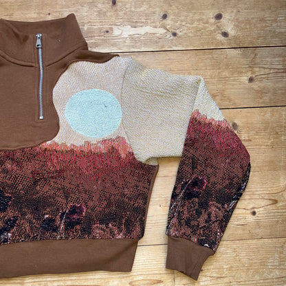 Detailansicht Vorderseite – handvernähtes Solar Flower Motiv mit Blumenwiese und hellblauer Sonne auf braunem Secondhand-Pullover von Sun Seam Studio, Recrafted Kollektion