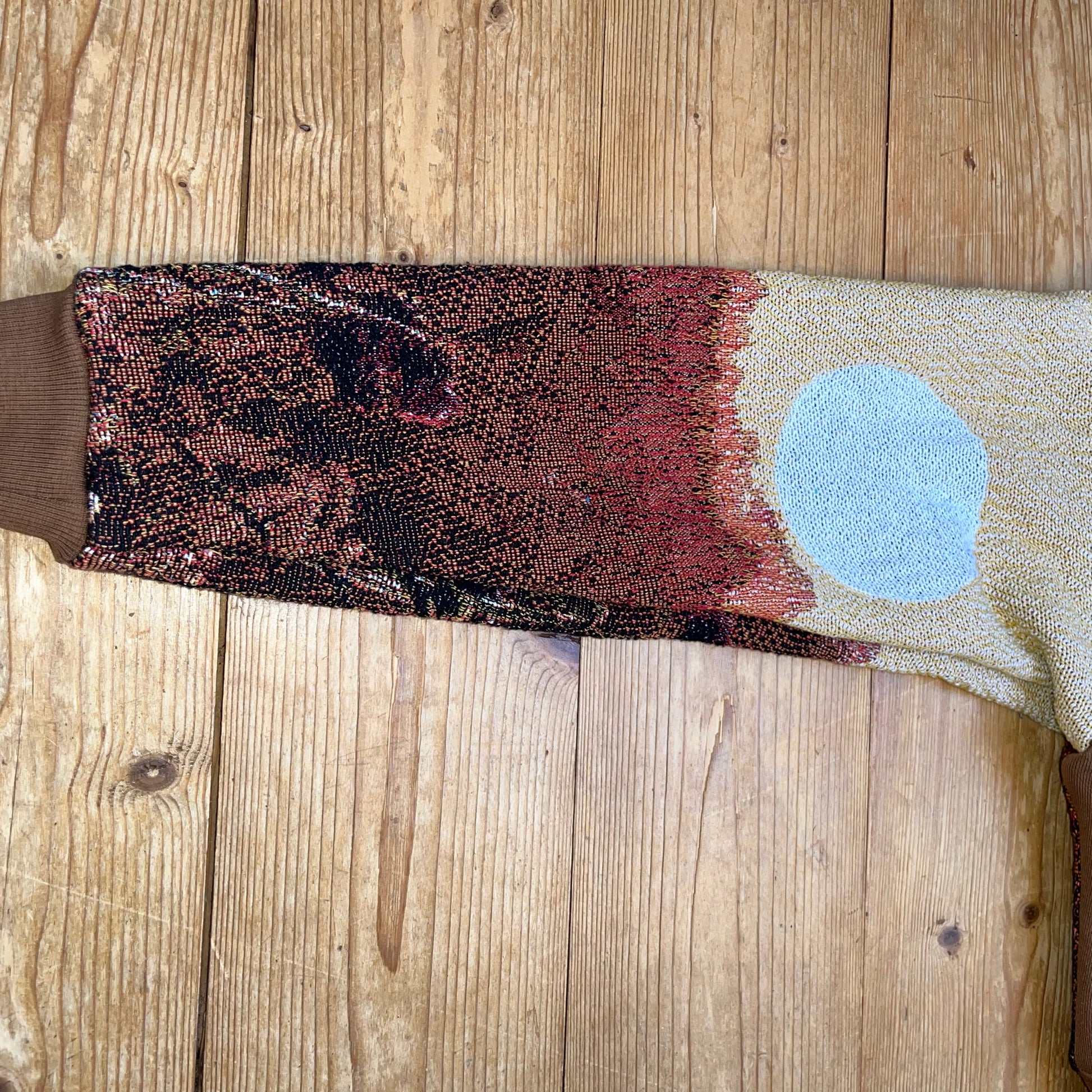 Ärmel-Detail des Solar Flower Motivs – gewebte Textur mit Blumenfeld und beigem Sonnenkreis auf dem Recrafted Secondhand-Pullover von Sun Seam Studio